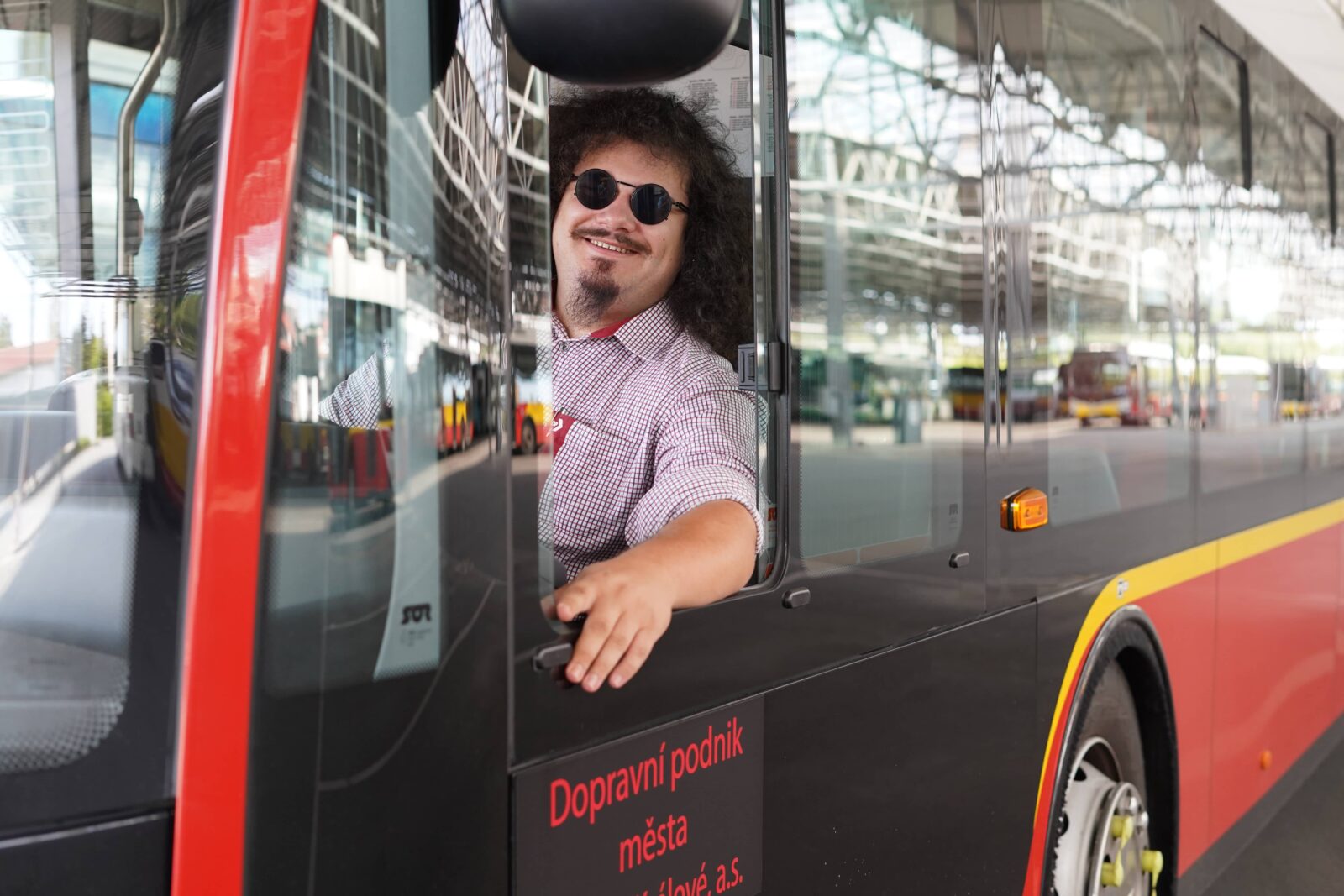 Smějící se řidič v kabině vozu MHD mávající z bočního otevřeného okýnka