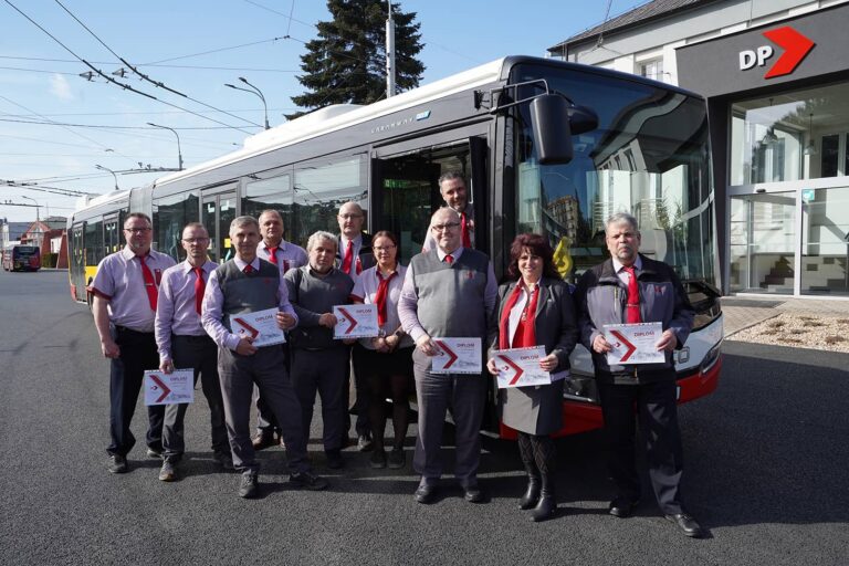 Skupinový snímek oceněných řidičů u kloubového autobusu před budovou dispečinku