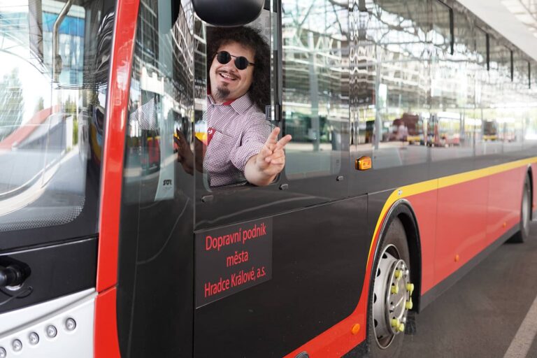 Smějící se řidič v kabině vozu MHD mávající z bočního otevřeného okýnka
