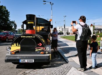 Maminka s dětmi si fotí čelo turistického vláčku DPMHK na zastávce v centru města během slunného dne.